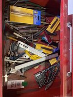 Drawer filled with assorted metal punches, rulers, and various hand tools including an auto center punch in packaging and measuring rulers.