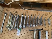 Wide view of multiple socket wrenches and combination wrenches organized on a pegboard with hooks.