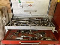Opened metal chest filled with assorted socket wrench tools and attachments, close view of tools in top and middle trays
