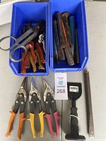 Blue containers with assorted tin snips, chisels, and hand tools including a metal file and black handled scraper