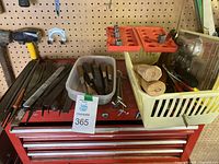 Wide shot of assorted tools laid out on a red tool chest and in baskets including files, chisels, screwdrivers and sockets.
