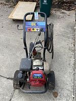 Front view of pressure washer on concrete showing metal frame, wheels, engine