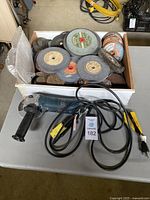 Bosch angle grinder and box filled with various grinder discs of different types and sizes on table