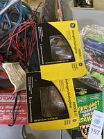 Photo showing two boxed General Electric Halogen H506 headlights among various car accessories such as cables and other automotive parts.