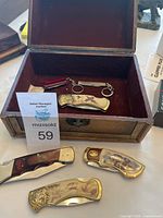 Photo of open wooden box with four knives inside and two knives outside, showing variety of designs and handle materials.