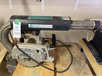 Side view of DeWalt radial arm saw showing blade and arm with label.
