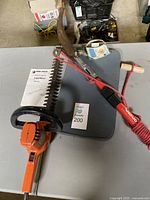 Top view of Black & Decker hedge trimmer next to metal branch trimmer and knee pad on a table.
