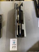 Torque wrench inside gray molded plastic case on a gray surface alongside auction lot card 211.