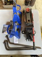 View of hydraulic floor jack, two blue jack stands, and three metal handles on a table.