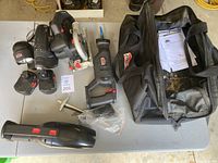 All cordless tools, batteries, charger, and carrying bag laid out on table.