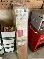 Multiple boxes of vinyl flooring planks stacked against a wall with shrink-wrap intact. One box shows the Take-Off brand and cherry wood color image.