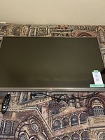Front view of LG 42-inch TV lying flat on patterned carpet, showing screen and thin bezel, with auction tag labeled 50.