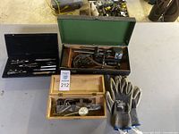Overview of wooden and green tool cases with machinist measuring and layout tools and safety gloves on a table.