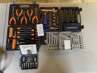 Full overview showing two black plastic tool cases with multiple orange and blue handled tools inside along with separate small clear cases containing drill bits and sockets.