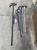 Full view of all 10 metal and wood hand tools laid on concrete, showing pipe bender, sledgehammer, multiple crow bars and hand screwdrivers.