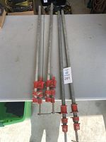 Four pipe clamps on table; two shorter, two longer with red clamp heads.