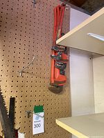 Photo showing three orange pipe wrenches hanging on a pegboard wall with visible wear and rust.