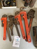 Seven pipe wrenches arranged on a table, showing variation in size and condition, with a mix of red painted and rusted metal finishes.