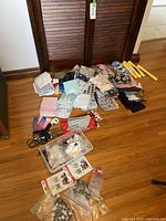 Overview of fabric pattern pieces folded and stacked, rotary cutting tool, and plastic bin with buttons on wooden floor