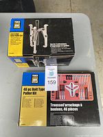 Two puller kits on a table: a 4-piece 3-jaw gear puller set box and a 46-piece bolt type puller kit box with visible tools.