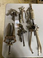 Full view of six various sized pullers arranged on a table, showing different types and sizes with mechanical screw mechanisms and gripping hooks.