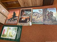 Four posters laid out on floor: three Remington rifle posters showing different hunting scenes and one sport fish guide poster