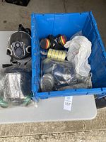 Photo showing blue plastic container filled with several respirators and filter cartridges, and plastic wrapped additional mask.