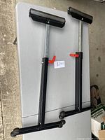 Pair of two adjustable roller stands shown side by side on a table, with black bases, silver uprights, red locking levers, and padded tops.