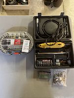 Full lot on table including yellow rotary tool, black case with accessories, clear plastic bit box, and bag of small accessories