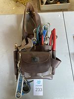 Top view of brown leather tool belt with assorted hand tools inside compartments and loops