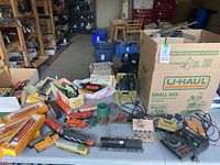Overview of assorted HO scale train items including locomotives, tracks, motors, and controllers spread on table with storage boxes visible in background.
