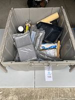 Large beige plastic container filled with painting supplies including paint rollers, paint trays, brushes, and other tools.