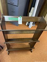 Front view of the wooden bookshelf showing three shelves, dark brown finish, and raised edges on shelves.