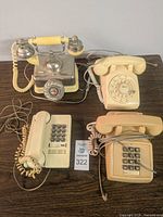 Lot of four vintage telephones, two rotary dial and two push-button models, placed on a table with cords visible.