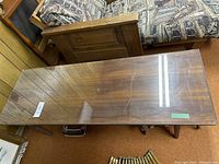 View of entire rectangular teak table with glass top, surrounded by furniture and carpeted floor.