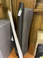 Three rolls of vinyl standing upright against wood-paneled wall, showing grey and black material rolls.