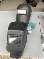 Two black welding helmets placed on a table, showing the shape and protective glass windows