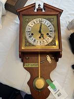 Full view of wooden wall clock with pendulum and winding key on tabletop.