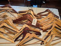 Photo showing a spread of wooden hangers in natural and dark wood finishes arranged on a light surface, approximately 50-60 pieces.