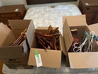 Three cardboard boxes filled with wooden and plastic hangers on a mattress.