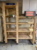 Full view of wooden shelving unit with heater on top shelf, showing all shelves and supporting wooden beams on caster wheels.