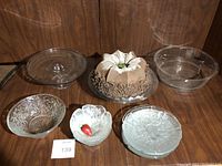 Full view of all items showing two glass cake plates, three small glass bowls/plates and foam cake replica on a glass plate
