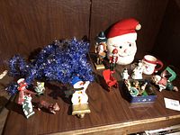 Photo showing the blue metallic tinsel garland, two wood nutcracker figurines, Santa ceramic ornament, snowman and other small assorted Christmas ornaments grouped on a wooden surface.