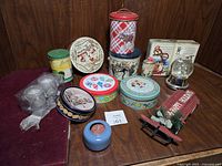 Overall view of lot showing Christmas tins, penny rolls, red sled, snow globe, and other small holiday decorations