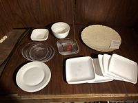 Top view of various white round and square plates, clear glass round and square plates, a white bowl, and an off-white floral patterned oval platter.