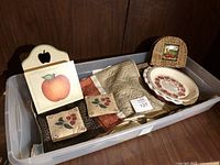 Photo showing a tray holding autumn-themed ceramic pie plates, coasters, wooden apple wall plaque, small woven picture frame, and folded quilted textiles