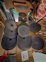 Used circular saw blades of varied sizes laid on cardboard inside a box, many showing signs of wear and some rust