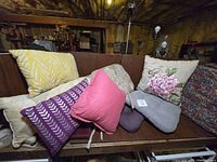 Wide view of assorted cushions and pillows stacked on wooden bench, showing variety of colors and patterns