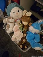 Various stuffed bunnies in mixed colors and sizes inside a blue storage bin.