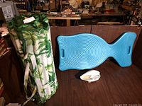 Two rolled inflatable pool floats with a tropical leaf pattern next to a large blue plastic fish-shaped float or tray on a wooden surface.